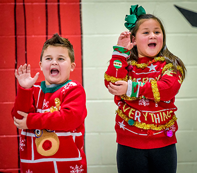 two kids in christmas sweaters using sign language