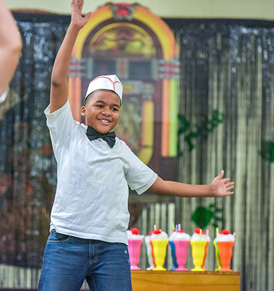 kid in soda jerk hat with arm in air